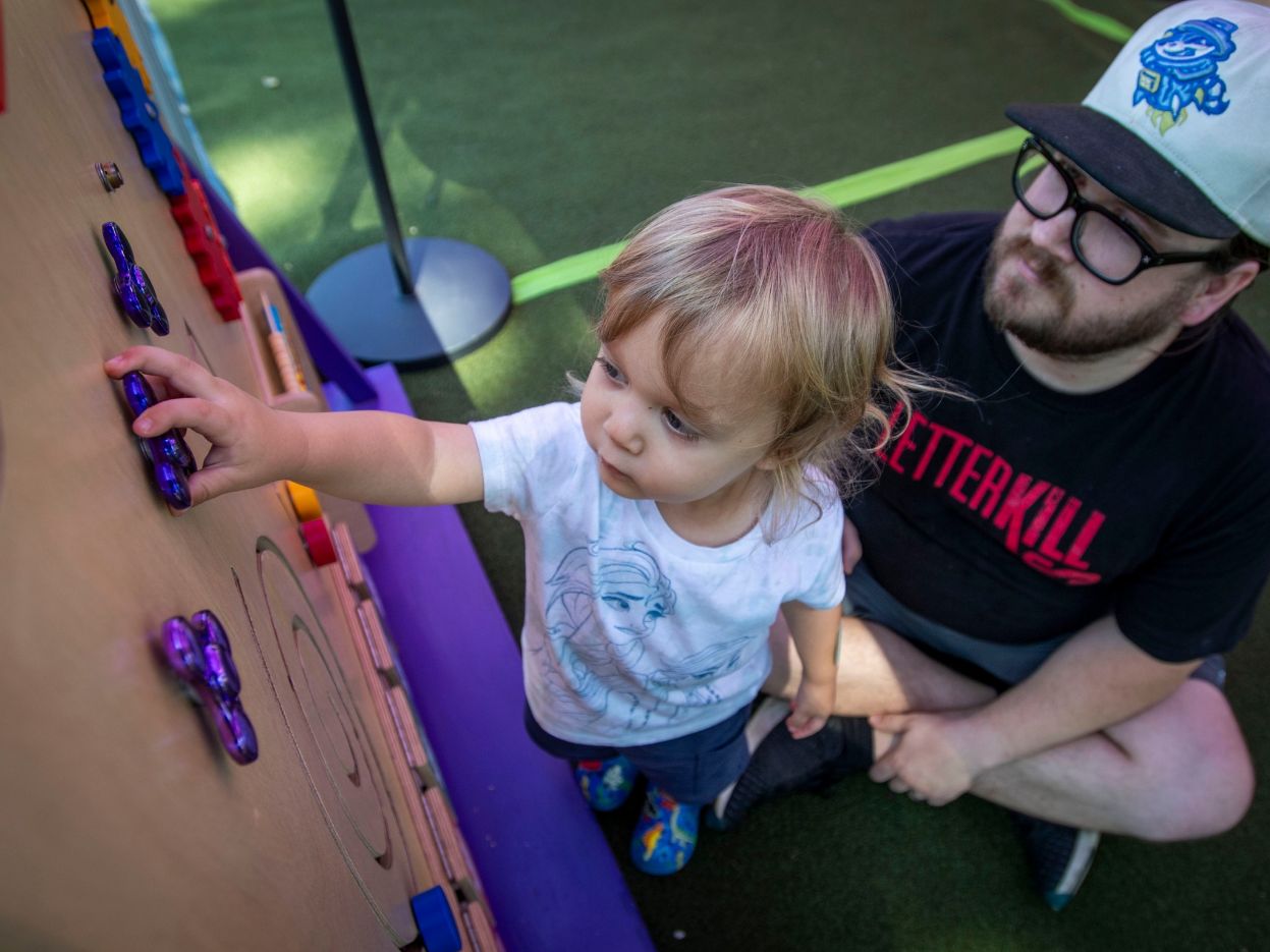 An adult and child exploring a colorful activity wall